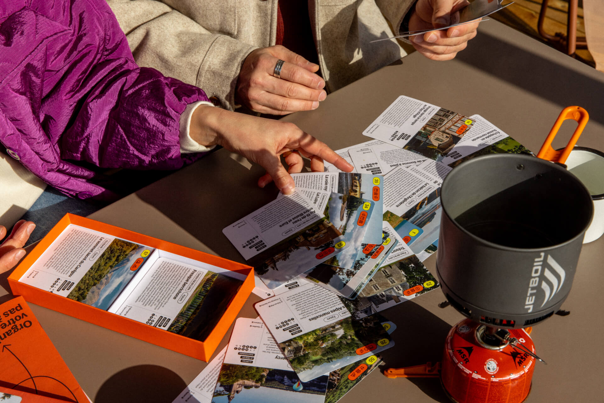 3S6A1076 Jeu de voyage avec des cartes étalées sur une table, un réchaud Jetboil et le livre « Organisez votre voyage » du Bon Air Club.