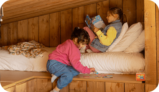 IMAGE-FAMILLE-1 Deux filles lisant et jouant dans une chambre mansardée confortable aux murs en bois.