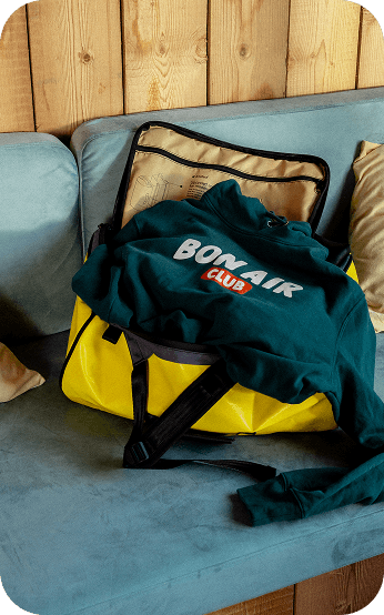 Sac de sport jaune contenant un sweat à capuche « Bon Air Club », posé sur un canapé bleu.