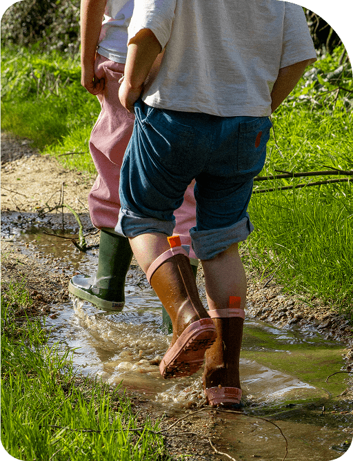 Des enfants en bottes de pluie éclaboussant dans une flaque boueuse, profitant des jeux en plein air.